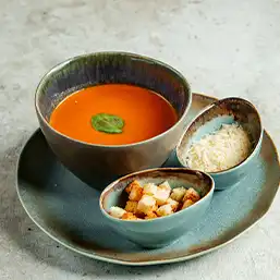 A bowl of delicious soup with side serving of croutons and herbs