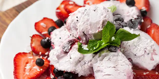 Bowl with two scoops of ice cream, black pepper flecks, and fresh sliced strawberries