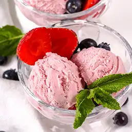 Bowl with two scoops of berry ice cream, garnished with sliced strawberries, blueberries, and mint