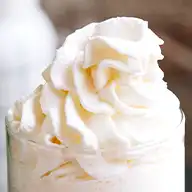 A perfect swirl of whipped cream on top of a glass of cold drink.