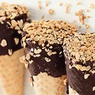 A trio of ice cream cones topped with a variety of chopped nuts