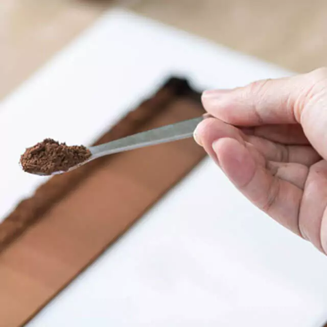 Hand holding a teaspoon filled with coffee