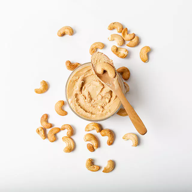 Above shot of cashew nut butter paste with raw cashews scattered on the side 